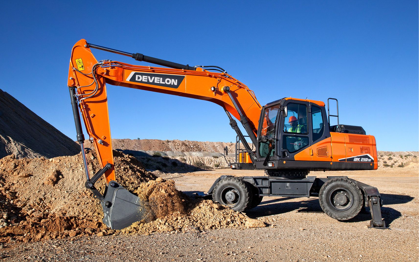 DEVELON -7 series wheel excavator bucket digs into the ground, while the outriggers stabilize the machine.