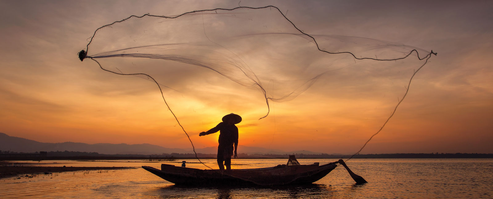 A fisherman in Myanmar throws their net at sunrise