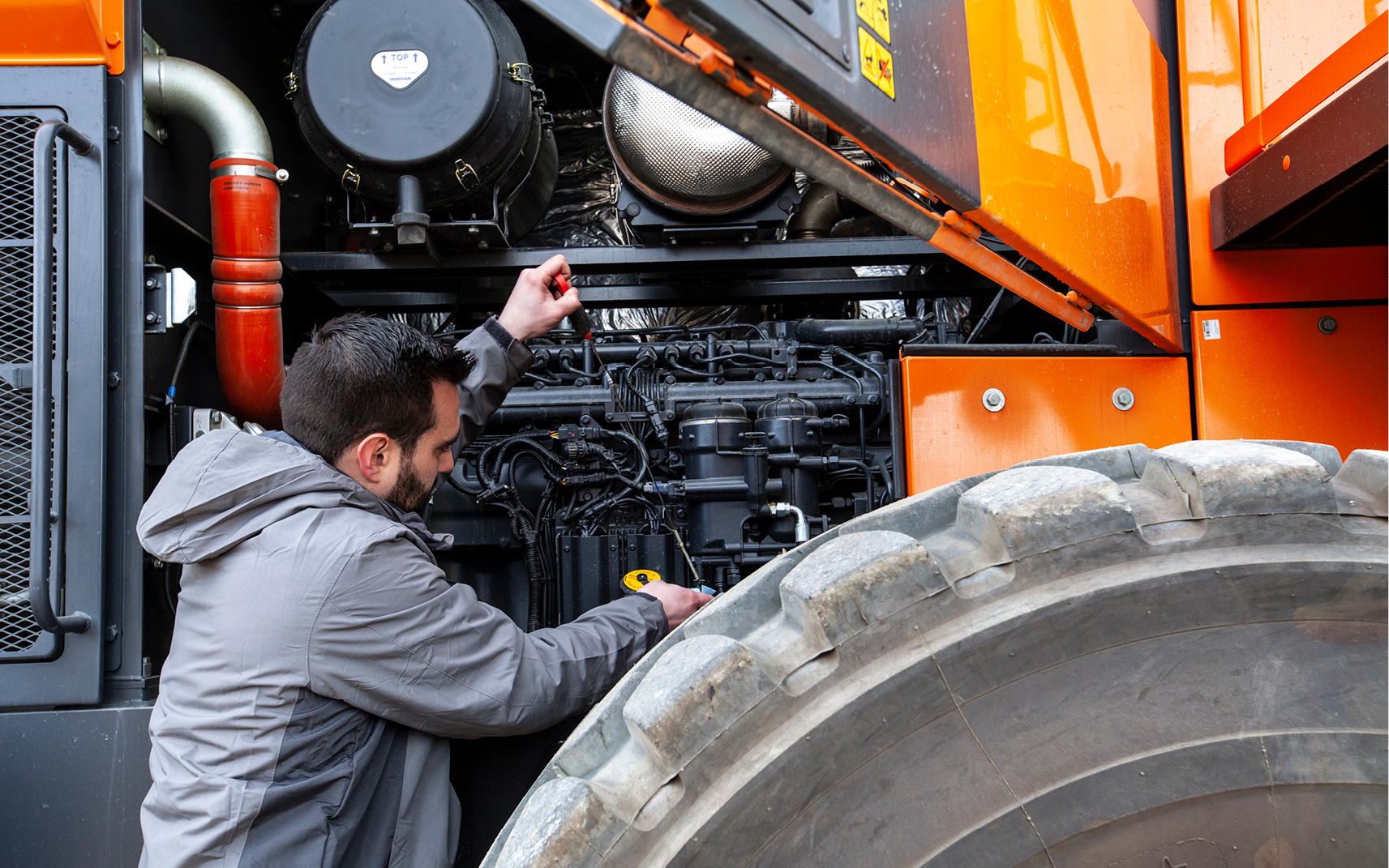 A DEVELON employee performs preventive maintenance on a -7 Series wheel loader.