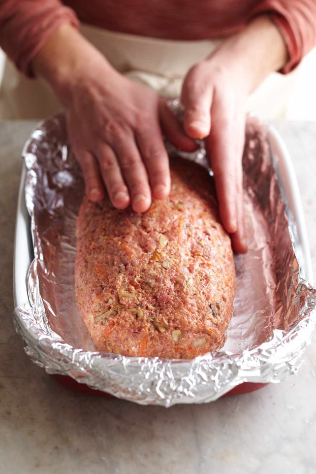 hands shaping meat into loaf on foil-lined baking pan