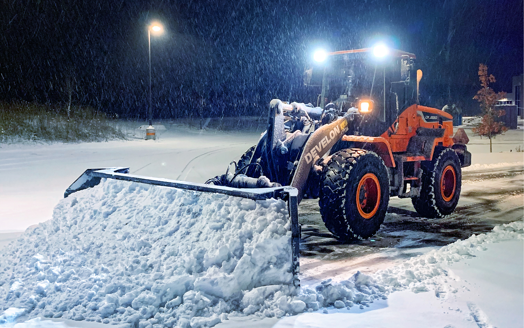 A DEVELON DL220 wheel loader pushing snow at night.