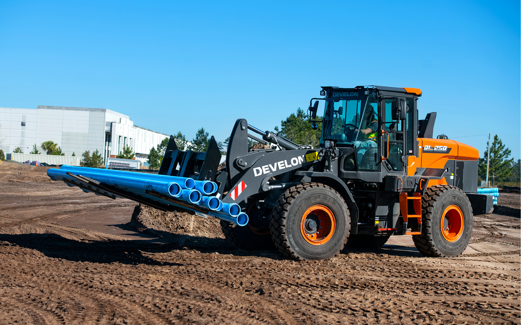 DEVELON wheel loader carries blue pipes across a jobsite. 