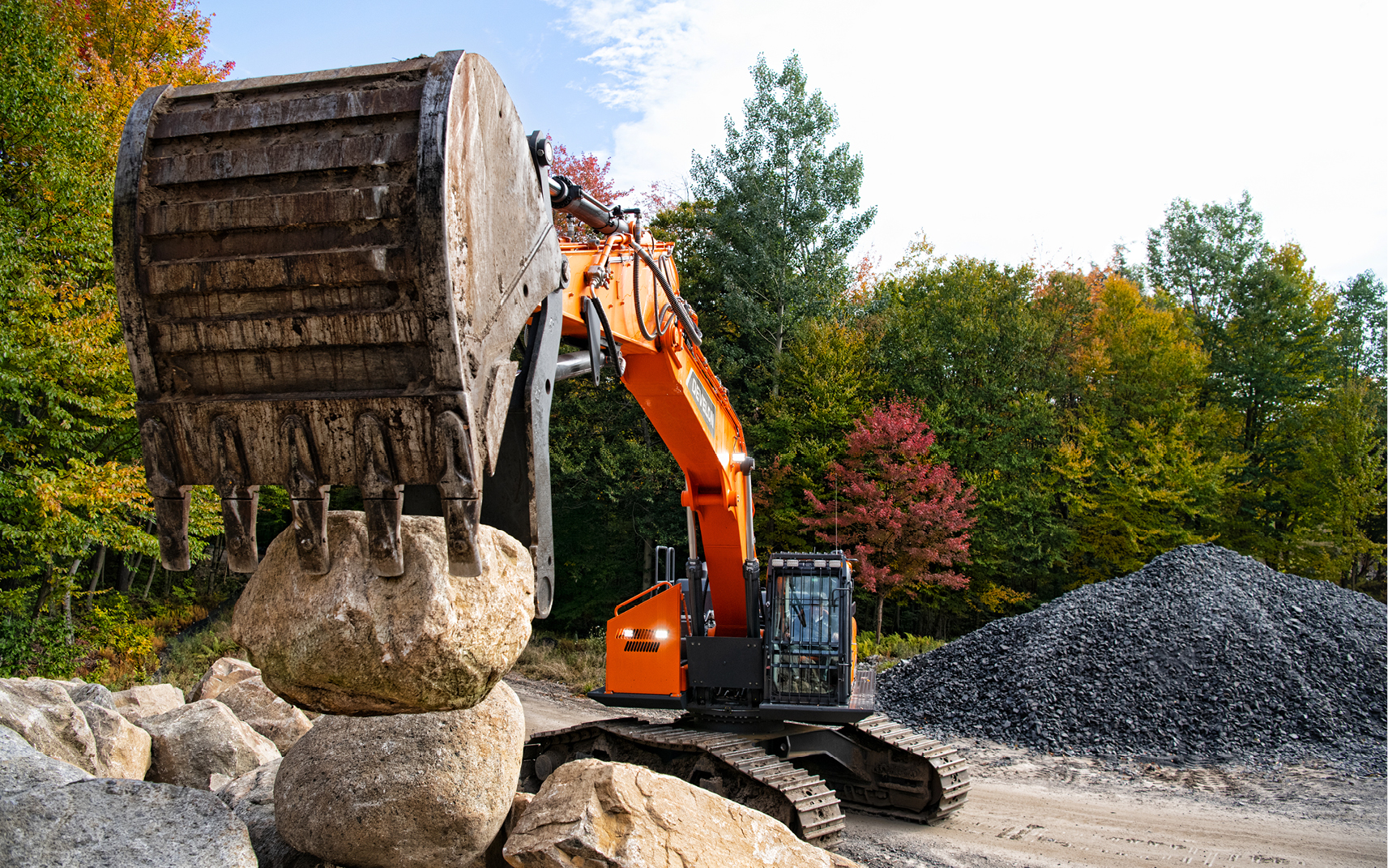 A DEVELON excavator lifts a boulder using bucket and thumb attachments.