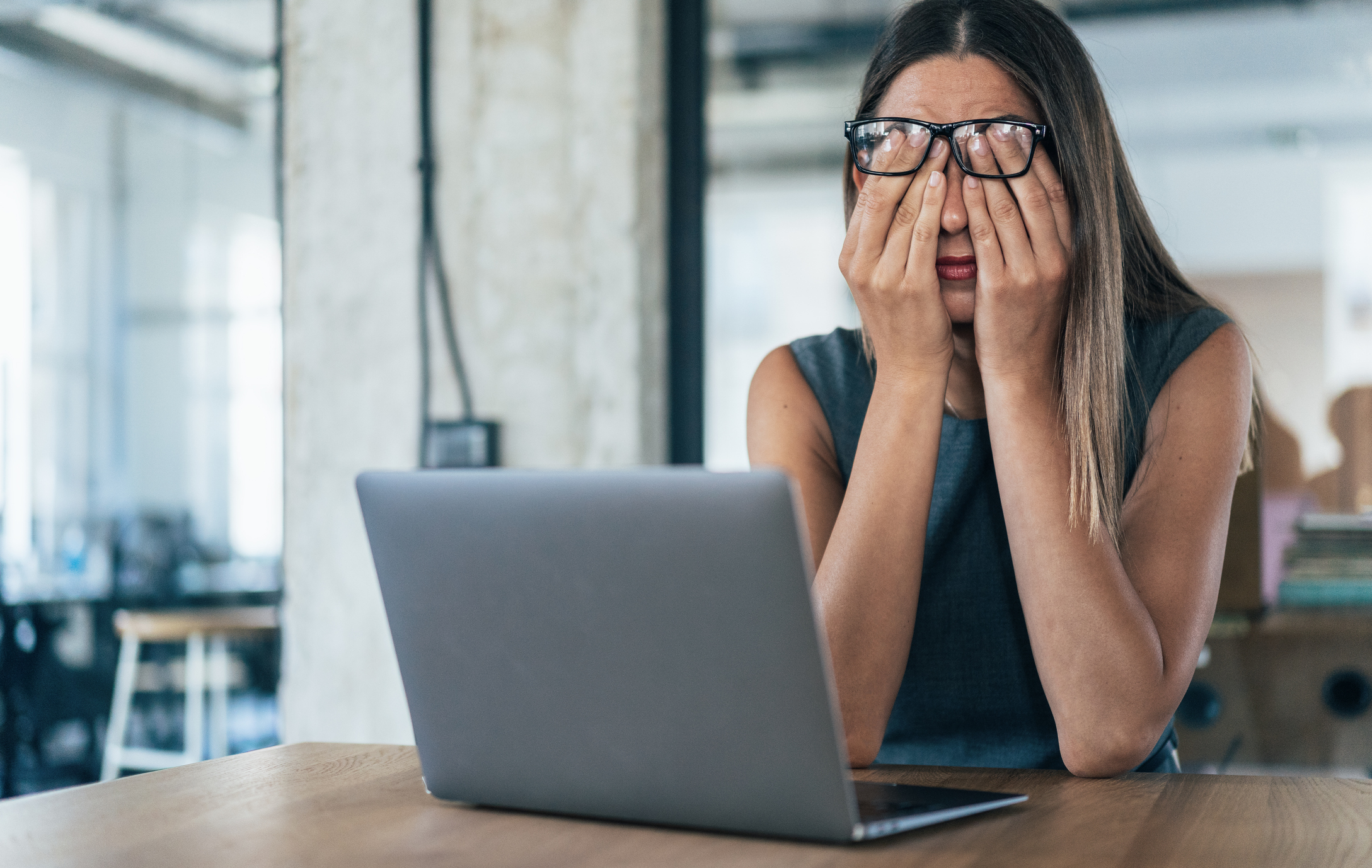 Weary person rubbing their eyes behind laptop